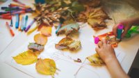 A photo of a preschool student gluing down leaves found outside for an art project