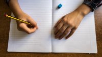 A photo of a student holding a pencil to blank notebook paper