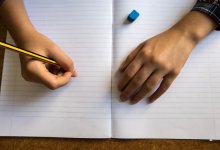A photo of a student holding a pencil to blank notebook paper
