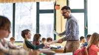 A photo of a teacher handing out papers to elementary students