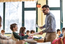 A photo of a teacher handing out papers to elementary students