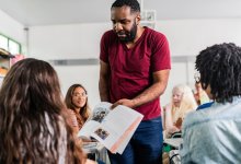 A photo of a teacher prompting his students to further analyze a textbook.