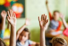 A photo of students in an elementary classroom raising their hands