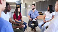 A photo high school students and their teacher sitting in a circle and talking