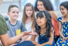 Elementary students listening to their teacher while sitting on the floor