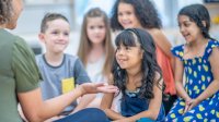 Elementary students listening to their teacher while sitting on the floor