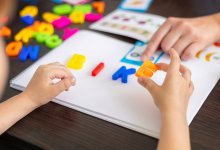 A photo of a kindergartener forming a word with magnetic letters with the guidance of a teacher