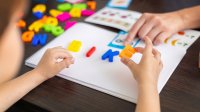 A photo of a kindergartener forming a word with magnetic letters with the guidance of a teacher