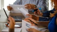 A meeting between school leaders and teachers using printed sheets and laptops