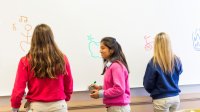 A photo of students standing at the board and drawing for a pictionary game