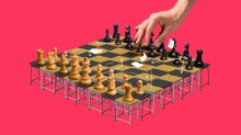 A hand reaching over a chess game with the board made of student desks