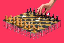 A hand reaching over a chess game with the board made of student desks