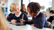 A photo of an elementary student using a tablet to explain a math problem to another student