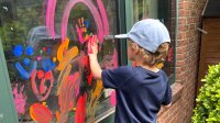 Elementary student finger painting on a window