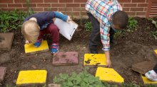 A photo of preschool students examining and turning over stepping stones outside
