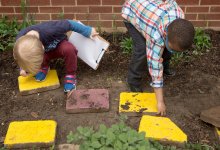 A photo of preschool students examining and turning over stepping stones outside