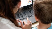 A photo of a teacher guiding an elementary student in a laptop program