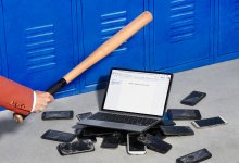 photo of a pile of broken cell phones with an open chromebook on top. An arm on the left of the image is seen holding a baseball bat, ready to break the laptop.