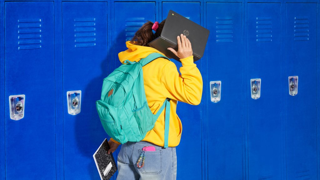 Student in hallway awkwardly holding up Chromebook to ear as if it were a cell phone.