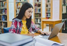 High school student completing research on a laptop in a library