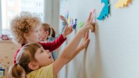 Preschool students picking out colors on a dinosaur banner