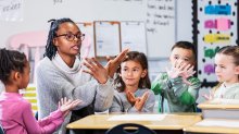 A teacher teaching her elementary students a hand motion in relation to a vocab word