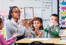 A teacher teaching her elementary students a hand motion in relation to a vocab word