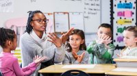 A teacher teaching her elementary students a hand motion in relation to a vocab word