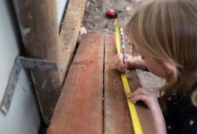An elementary student measuring a plank of wood outdoors