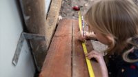An elementary student measuring a plank of wood outdoors