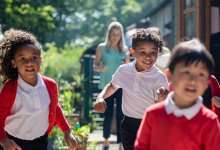 A photo of students excitedly running outdoors as their teacher observes from afar