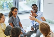 Photo of a circle of five students with teacher high-fiving one student