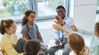 Photo of a circle of five students with teacher high-fiving one student