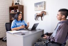 female teacher in Northern University shirt counsels an older student in her office
