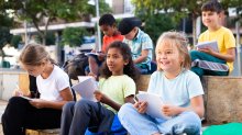 Elementary students sitting outdoors with notebooks and observing their surroundings