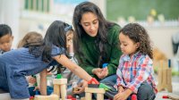 Preschool teacher playing with students while sitting on the floor