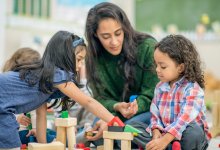 Preschool teacher playing with students while sitting on the floor