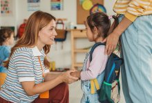 Preschool teacher kneeling down to welcome a student to class
