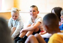 Elementary students sitting in a group on the floor listening to someone speaking