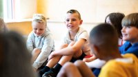 Elementary students sitting in a group on the floor listening to someone speaking