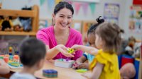 A teacher passing a preschool student a toy