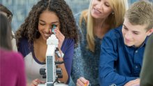 A teacher observing a group of high school students interested in examining material through a microscope