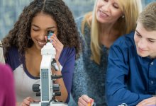 A teacher observing a group of high school students interested in examining material through a microscope