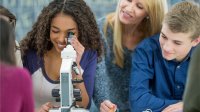 A teacher observing a group of high school students interested in examining material through a microscope