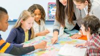 A group of students watching intently as their teacher points to sections on a map