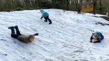 Elementary students sliding their bodies down a snowy hill