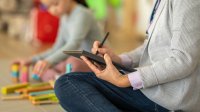 Teacher taking notes on a tablet while observing student