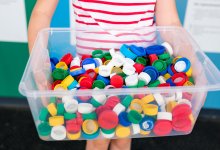 An elementary student holding up a bin full of plastic lids