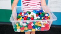 An elementary student holding up a bin full of plastic lids