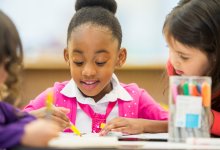 A small group of elementary students writing together on the same piece of paper